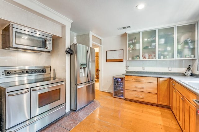 kitchen with beverage cooler, stainless steel appliances, visible vents, light wood-style floors, and glass insert cabinets