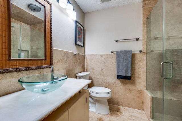 bathroom with tile walls, vanity, a textured ceiling, a shower with shower door, and toilet