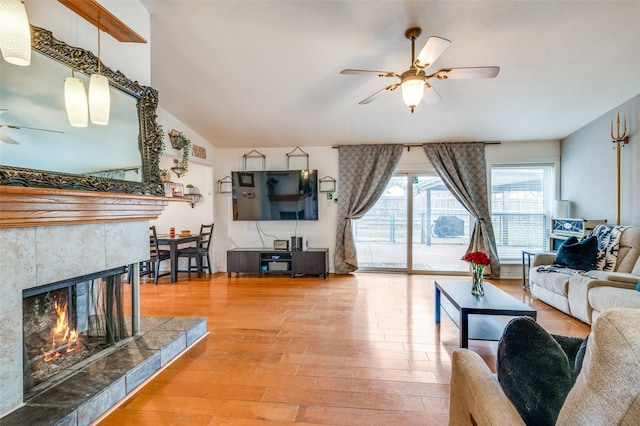 living room with a tiled fireplace, wood-type flooring, lofted ceiling, and ceiling fan