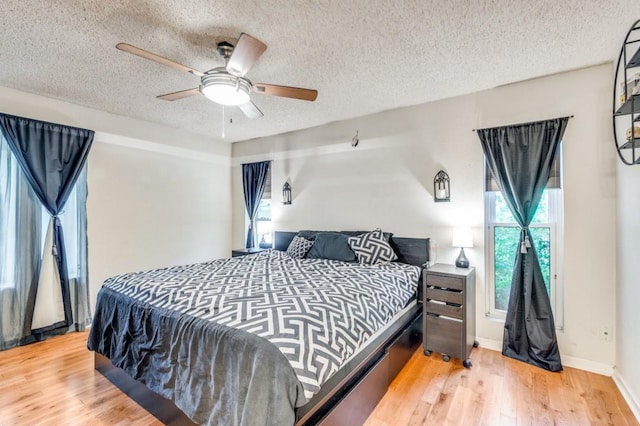bedroom with light wood-type flooring, a textured ceiling, a ceiling fan, and baseboards