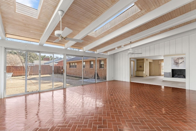 interior space with beamed ceiling, ceiling fan, a skylight, and a brick fireplace