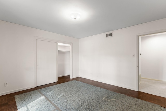 unfurnished bedroom featuring dark parquet floors and a closet