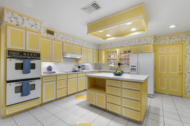 kitchen with a raised ceiling, a center island, light tile patterned floors, and white appliances