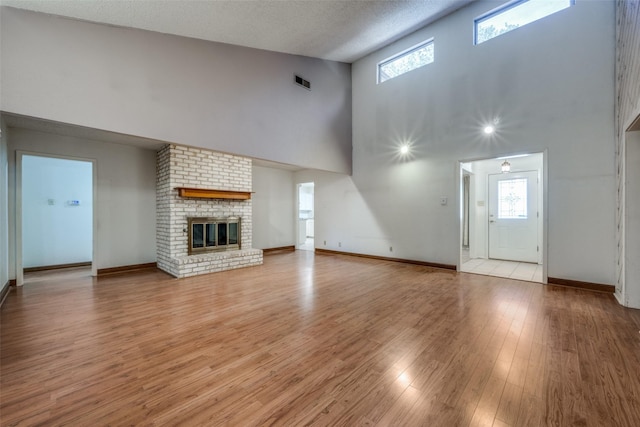 unfurnished living room featuring a brick fireplace, a wealth of natural light, a textured ceiling, and light hardwood / wood-style floors