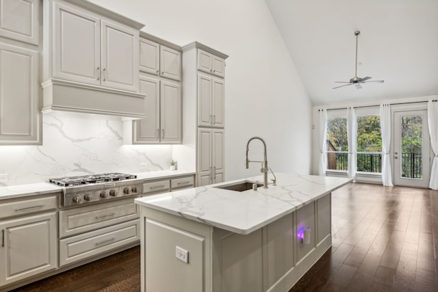 kitchen with vaulted ceiling, an island with sink, sink, stainless steel gas cooktop, and light stone countertops