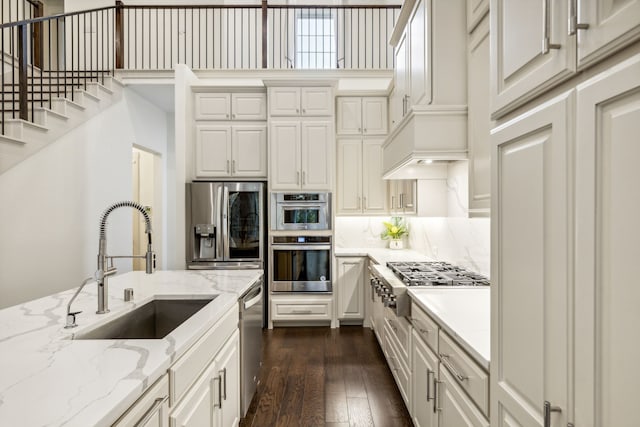 kitchen with sink, appliances with stainless steel finishes, white cabinetry, light stone counters, and dark hardwood / wood-style flooring