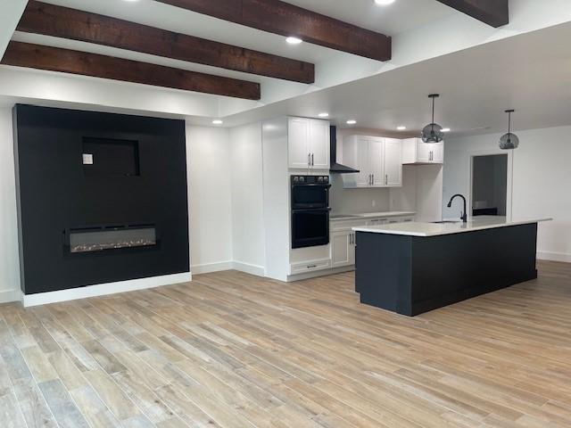 kitchen with white cabinetry, light hardwood / wood-style flooring, double oven, an island with sink, and pendant lighting