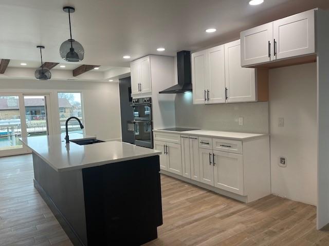 kitchen with sink, a center island with sink, white cabinets, and wall chimney exhaust hood