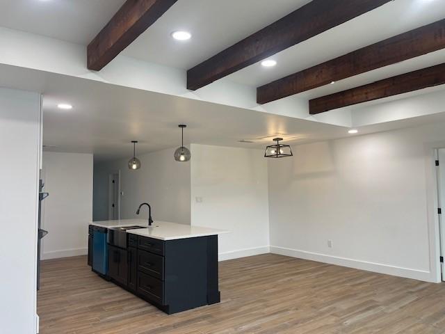 kitchen featuring sink, a center island with sink, hardwood / wood-style flooring, pendant lighting, and beam ceiling