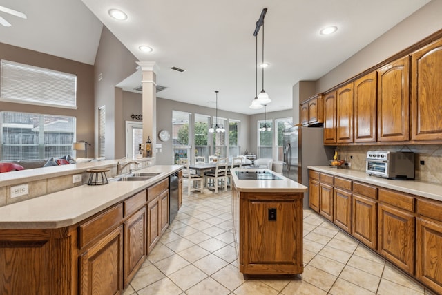 kitchen featuring decorative light fixtures, tasteful backsplash, an island with sink, decorative columns, and sink