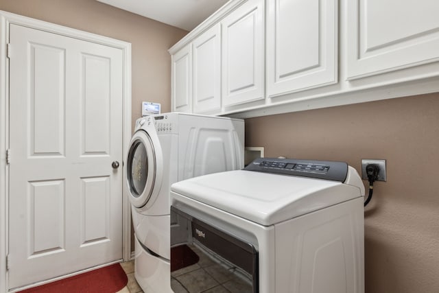 clothes washing area with tile patterned flooring, washer and clothes dryer, and cabinets