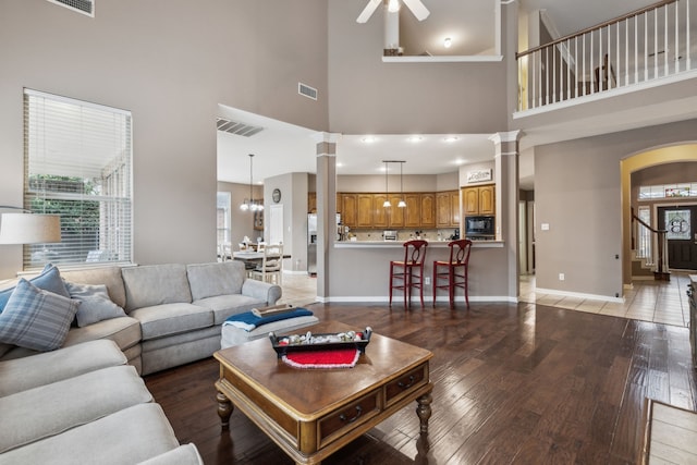 living room with ceiling fan, hardwood / wood-style floors, decorative columns, and a towering ceiling