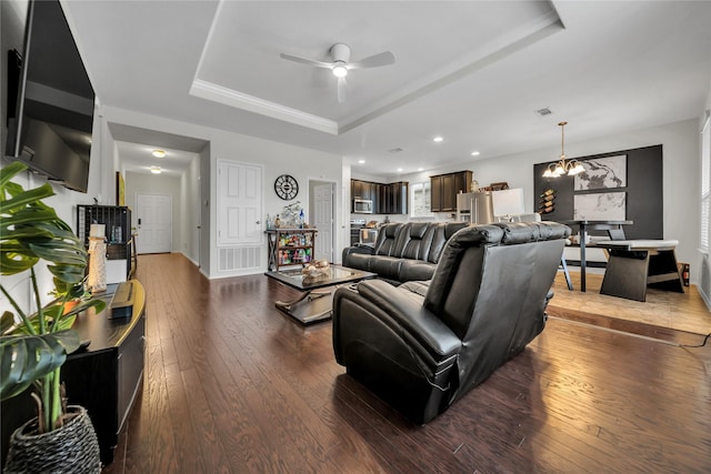 living room featuring a tray ceiling, dark wood-type flooring, and ceiling fan with notable chandelier