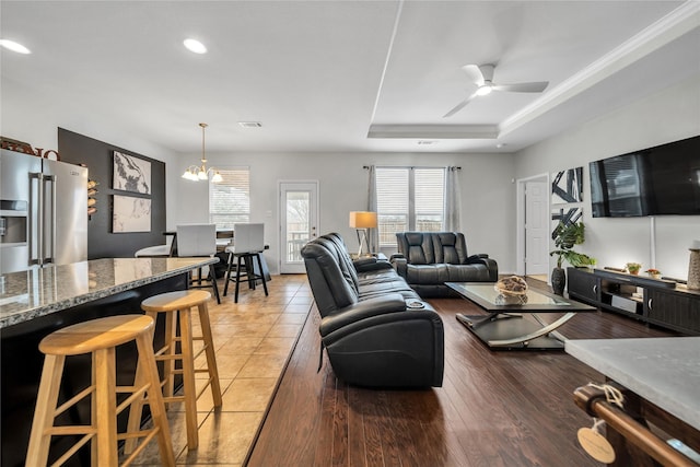 living room featuring a raised ceiling, hardwood / wood-style flooring, and ceiling fan with notable chandelier