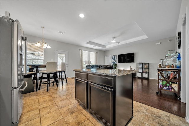 kitchen with light stone counters, decorative light fixtures, a center island, stainless steel refrigerator, and a tray ceiling