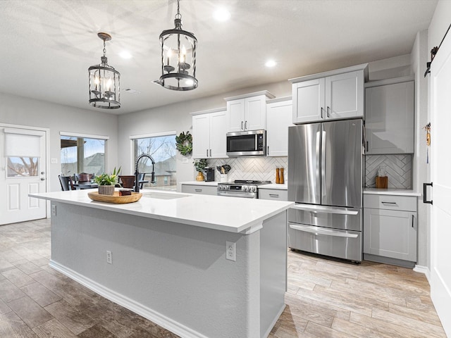 kitchen with sink, stainless steel appliances, a center island with sink, decorative light fixtures, and light wood-type flooring