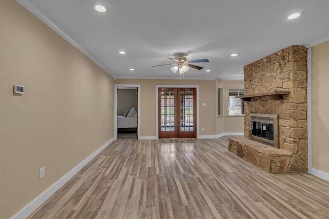 unfurnished living room with french doors, ornamental molding, a stone fireplace, and light hardwood / wood-style flooring