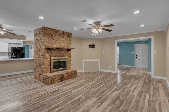 unfurnished living room featuring ceiling fan, ornamental molding, a stone fireplace, and light hardwood / wood-style flooring