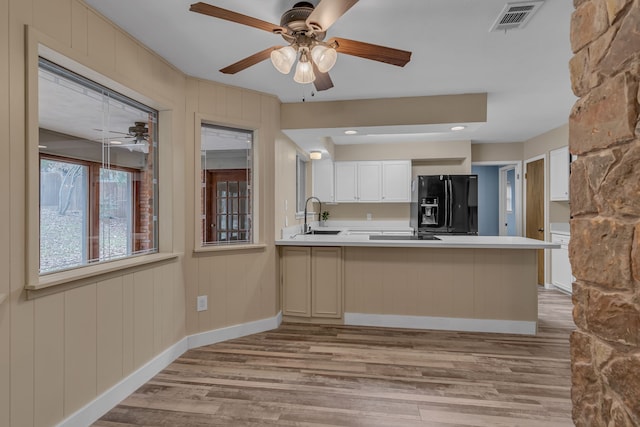 kitchen featuring light wood-type flooring, kitchen peninsula, black refrigerator with ice dispenser, and white cabinets