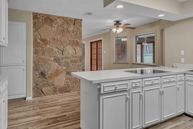 kitchen with black electric stovetop, kitchen peninsula, white cabinets, and light wood-type flooring