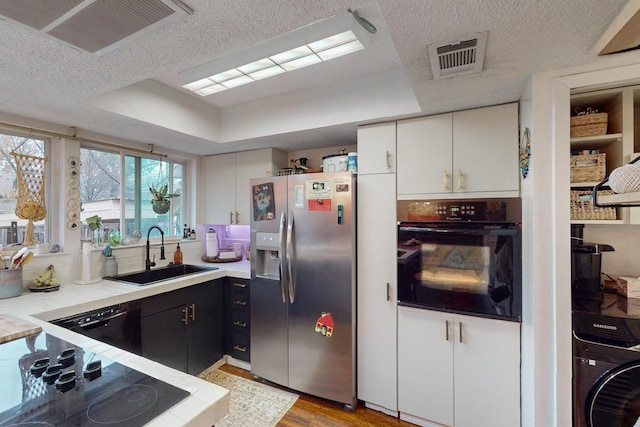 kitchen with black appliances, washer / dryer, sink, white cabinets, and a tray ceiling