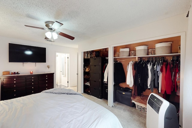 carpeted bedroom with ceiling fan, a textured ceiling, and two closets