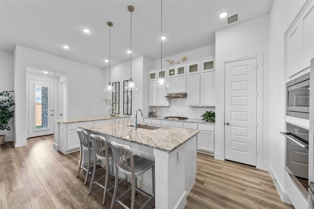 kitchen with sink, stainless steel appliances, light stone countertops, white cabinets, and a center island with sink