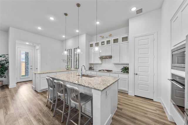 kitchen featuring sink, appliances with stainless steel finishes, a kitchen island with sink, white cabinetry, and light stone counters