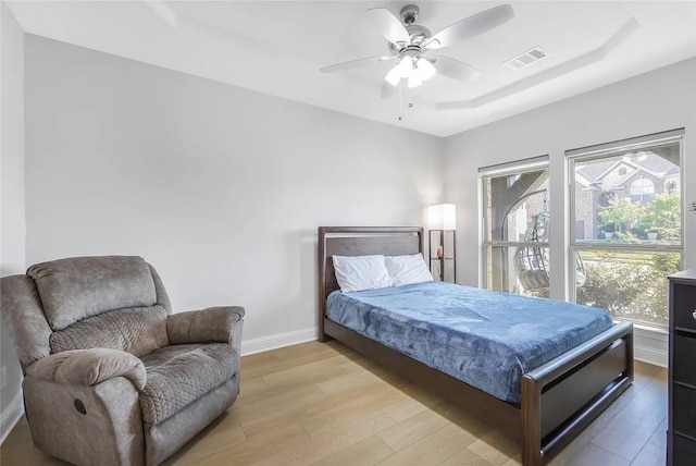 bedroom with a tray ceiling, light hardwood / wood-style floors, and ceiling fan