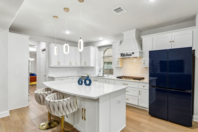 kitchen featuring a kitchen island, black refrigerator, decorative light fixtures, white cabinets, and custom range hood