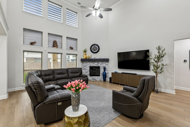 living room with a stone fireplace, ornamental molding, light hardwood / wood-style floors, and a towering ceiling