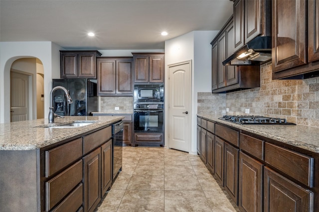 kitchen with sink, dark brown cabinets, tasteful backsplash, black appliances, and an island with sink