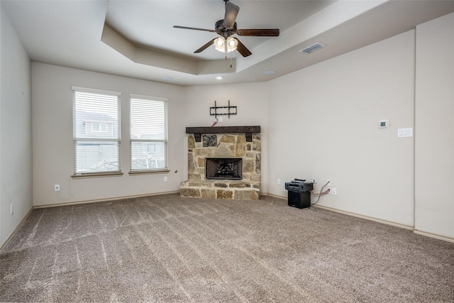 unfurnished living room featuring a raised ceiling, ceiling fan, carpet, and a fireplace