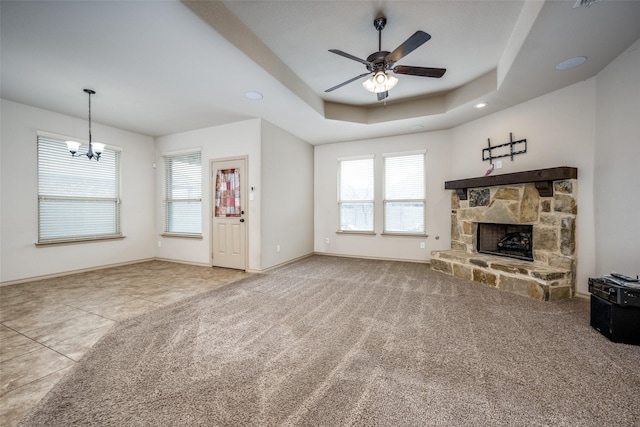 unfurnished living room with a raised ceiling, carpet, ceiling fan with notable chandelier, and a fireplace