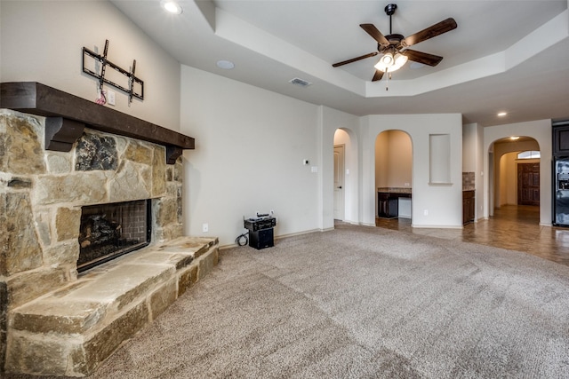 living room with ceiling fan, carpet flooring, a fireplace, and a tray ceiling