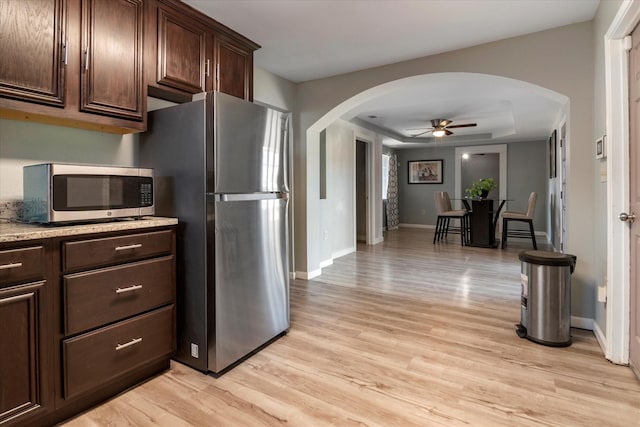 kitchen featuring stainless steel appliances, a raised ceiling, dark brown cabinets, and light hardwood / wood-style flooring