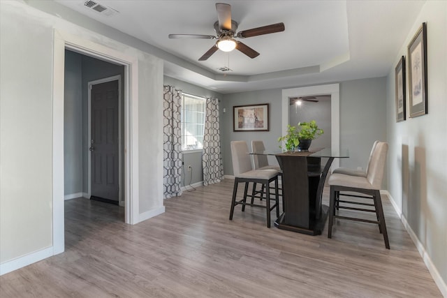 dining room with ceiling fan, a tray ceiling, and light hardwood / wood-style floors