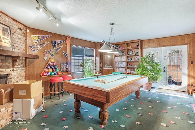 recreation room with wooden walls, carpet flooring, a textured ceiling, a brick fireplace, and french doors