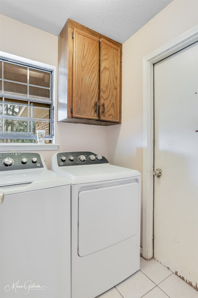 washroom with cabinets, washing machine and dryer, a textured ceiling, and light tile patterned floors