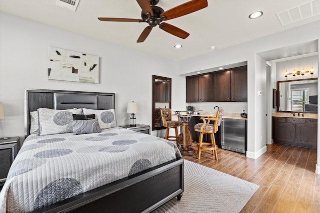 bedroom with ensuite bathroom, fridge, wet bar, and light hardwood / wood-style floors