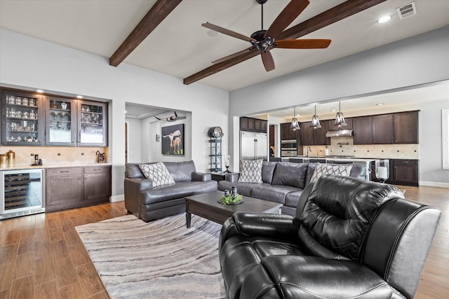 living room featuring hardwood / wood-style floors, indoor bar, wine cooler, ceiling fan, and beam ceiling