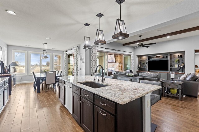 kitchen featuring sink, appliances with stainless steel finishes, hanging light fixtures, light stone counters, and a center island with sink