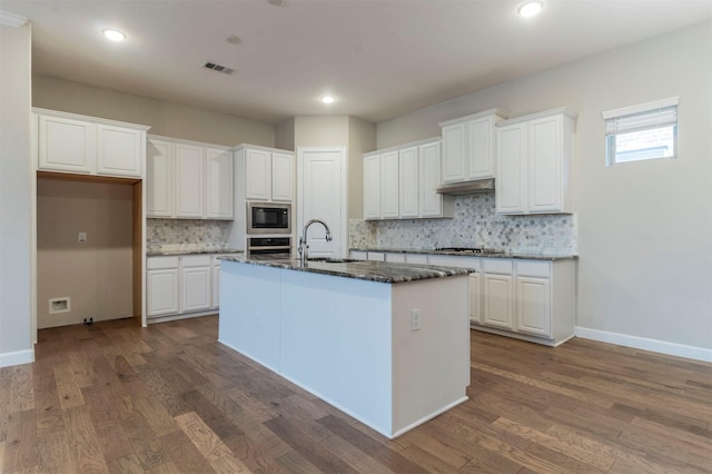 kitchen featuring sink, stainless steel appliances, an island with sink, white cabinets, and dark stone counters