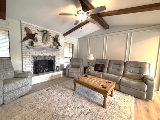 living room with ceiling fan, a fireplace, light hardwood / wood-style floors, and vaulted ceiling with beams