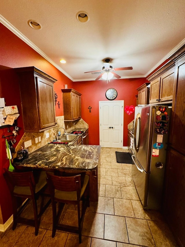 kitchen featuring sink, tasteful backsplash, ornamental molding, stainless steel fridge, and a kitchen breakfast bar