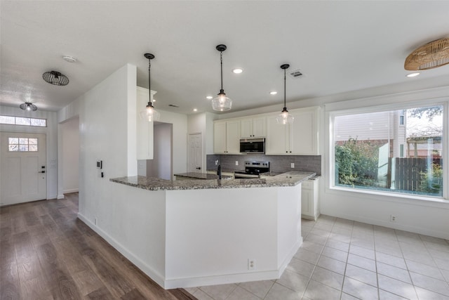 kitchen with tasteful backsplash, white cabinetry, dark stone counters, kitchen peninsula, and stainless steel appliances