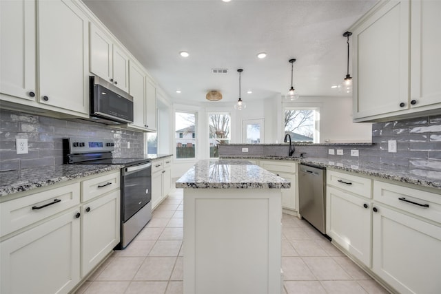 kitchen with light stone counters, decorative light fixtures, a center island, appliances with stainless steel finishes, and white cabinets