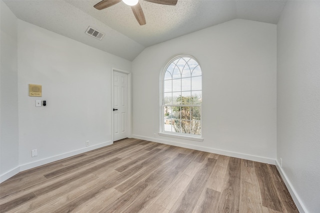 spare room featuring lofted ceiling, light hardwood / wood-style floors, and a textured ceiling