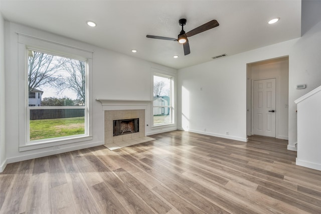 unfurnished living room featuring a tiled fireplace, a healthy amount of sunlight, and light wood-type flooring