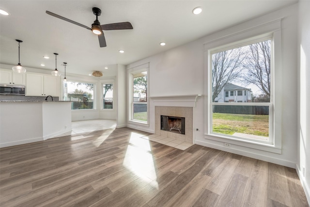 unfurnished living room with plenty of natural light, a tiled fireplace, and light wood-type flooring